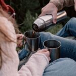 屋外でボトルからカップに飲み物を注ぐ手元