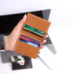 ノートパソコンの前でカードを収めた本革財布を手に持つ様子
