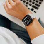 ノートパソコンの前で白いバンドのApple Watchを着けた手首