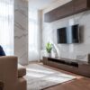 大理石調の壁に掛けたテレビと木目のロータイプのテレビボードがあるリビング