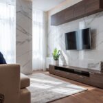 大理石調の壁に掛けたテレビと木目のロータイプのテレビボードがあるリビング