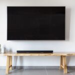 白い壁に掛けた大型テレビと、下の木のベンチに置いたサウンドバー