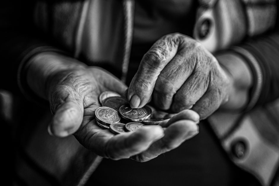 年配の人が手のひらに硬貨をのせて数える白黒写真