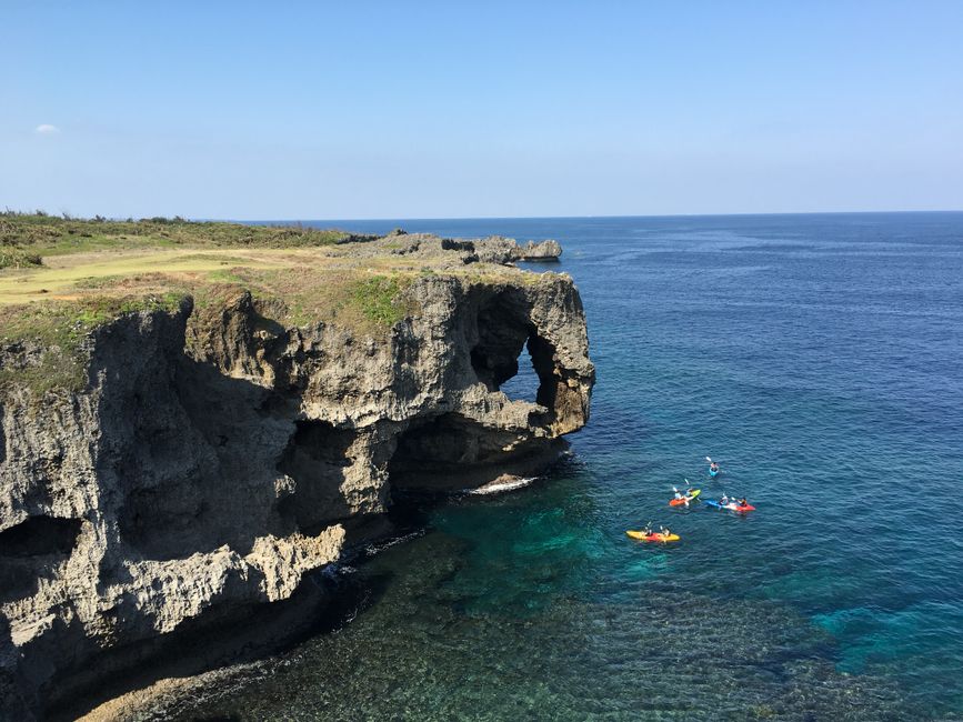 切り立った崖の下の青い海でカヤックを楽しむ人たち