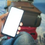 空港で旅行用バッグの上にスマートフォンを持つ手元
